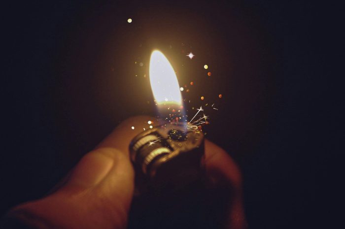 Intense close-up of a lighter igniting a bright flame with spark effects against a dark background.